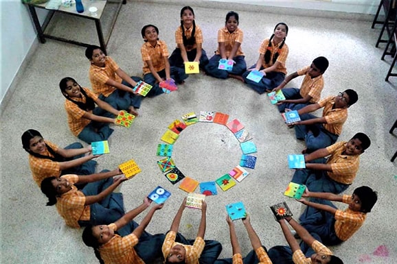 A group of school children sitting in a circle hold out brightly coloured tactile tiles. A smaller circle of tactile tiles are visible in the centre.