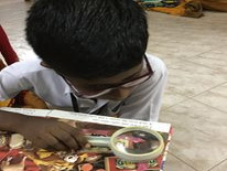 A boy uses a magnifying glass to see a picture in a book.